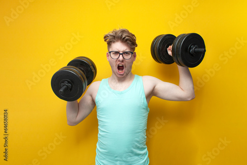 confident guy student lifts heavy dumbbells on a pink background, motivated nerd in glasses goes in for sports