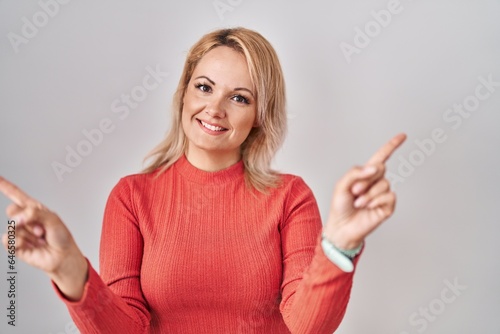 Blonde woman standing over isolated background smiling confident pointing with fingers to different directions. copy space for advertisement