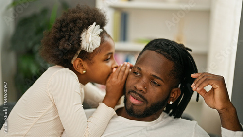 African american father and daughter sitting on sofa telling secret at home