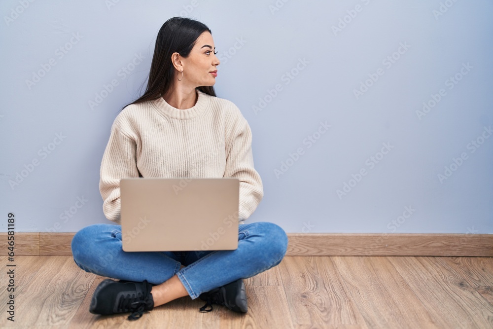 Young woman using laptop sitting on the floor at home looking to side, relax profile pose with natural face and confident smile. Young woman using laptop sitting on the floor at home looking to side, relax profile pose with natural face and confident smile.