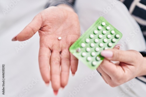 Young caucasian woman holding birth control pills at bedroom