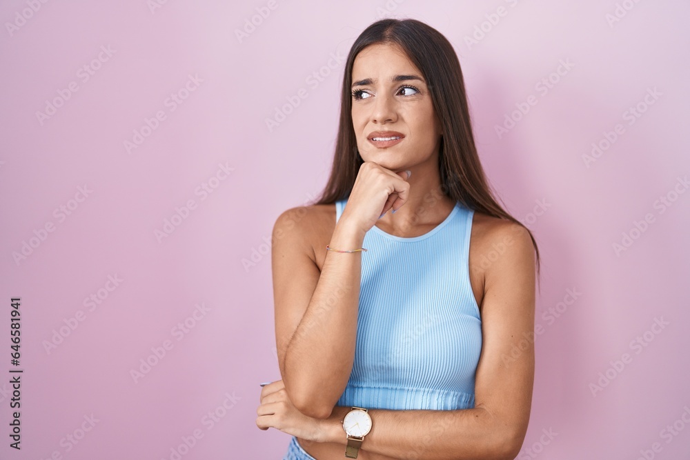 Fototapeta premium Young brunette woman standing over pink background thinking worried about a question, concerned and nervous with hand on chin