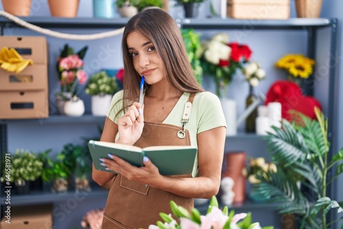 Young beautiful hispanic woman florist reading notebook with doubt expression at flower shop