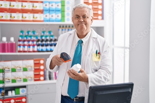 Middle age grey-haired man pharmacist scanning pills bottle at pharmacy