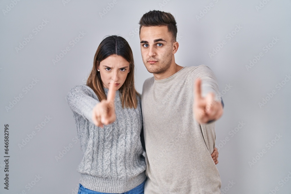 Young hispanic couple standing over white background pointing with finger up and angry expression, showing no gesture Young hispanic couple standing over white background pointing with finger up and angry expression, showing no gesture