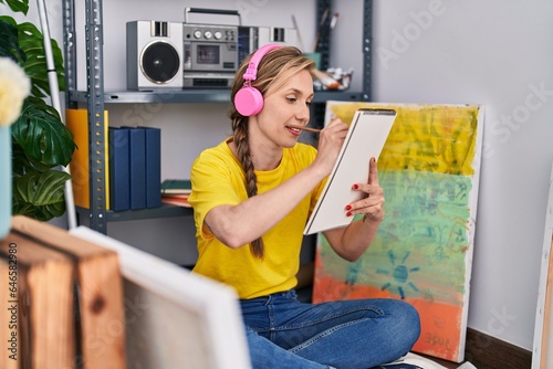 Young blonde woman artist listening to music drawing on notebook at art studio