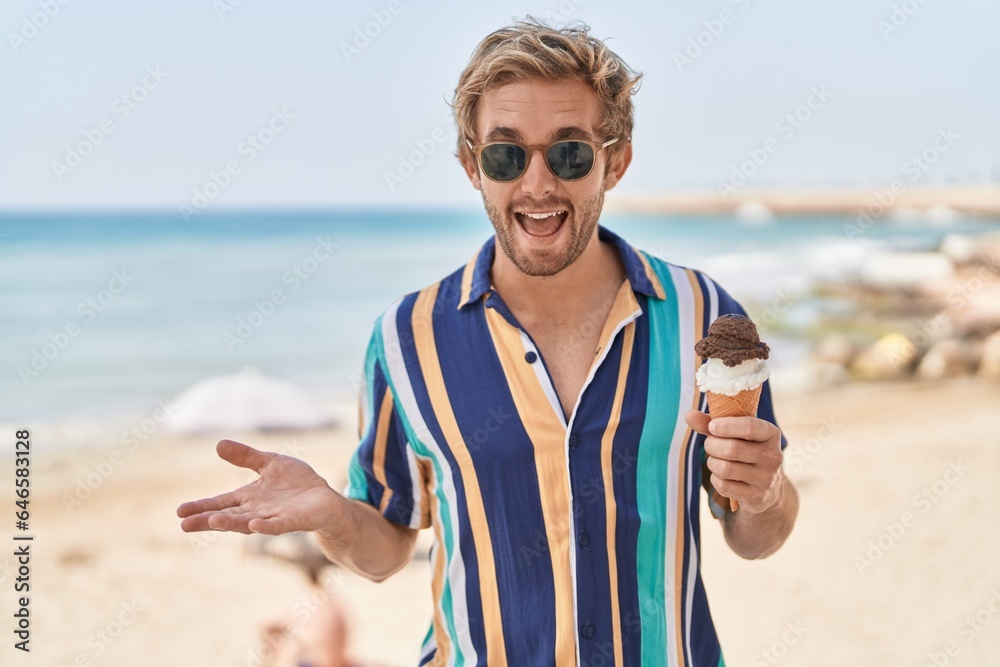 Caucasian man eating an ice cream at the beach celebrating achievement with happy smile and winner expression with raised hand