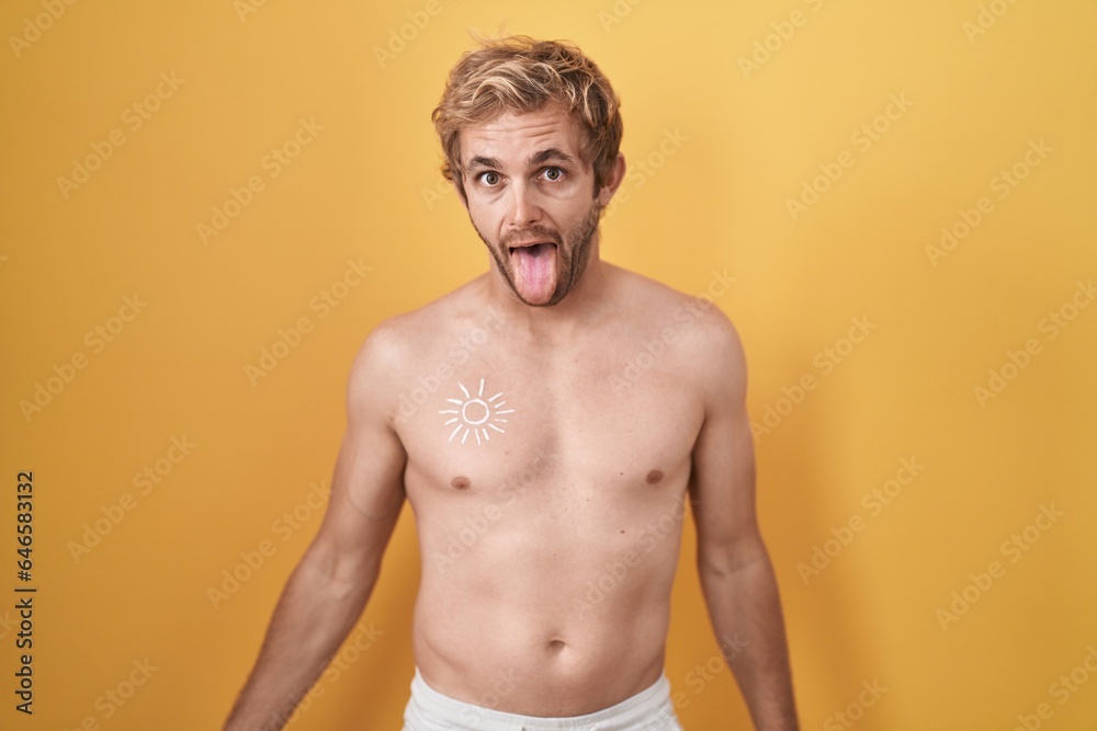 Fototapeta premium Caucasian man standing shirtless wearing sun screen sticking tongue out happy with funny expression. emotion concept.