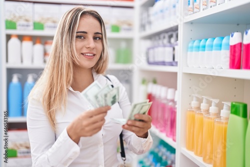 Young blonde woman customer smiling confident counting dollars at pharmacy