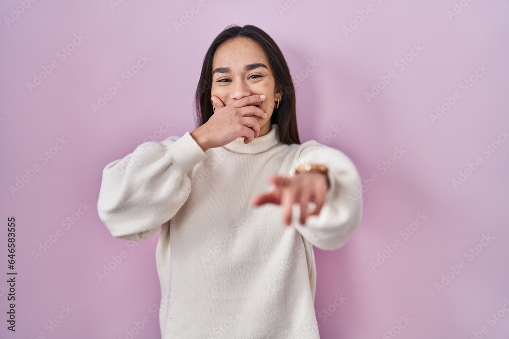 Young south asian woman standing over pink background laughing at you, pointing finger to the camera with hand over mouth, shame expression Young south asian woman standing over pink background laughing at you, pointing finger to the camera with hand over mouth, shame expression