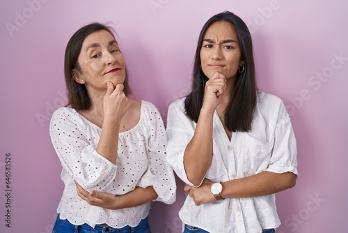 Hispanic mother and daughter together looking confident at the camera smiling with crossed arms and hand raised on chin. thinking positive.