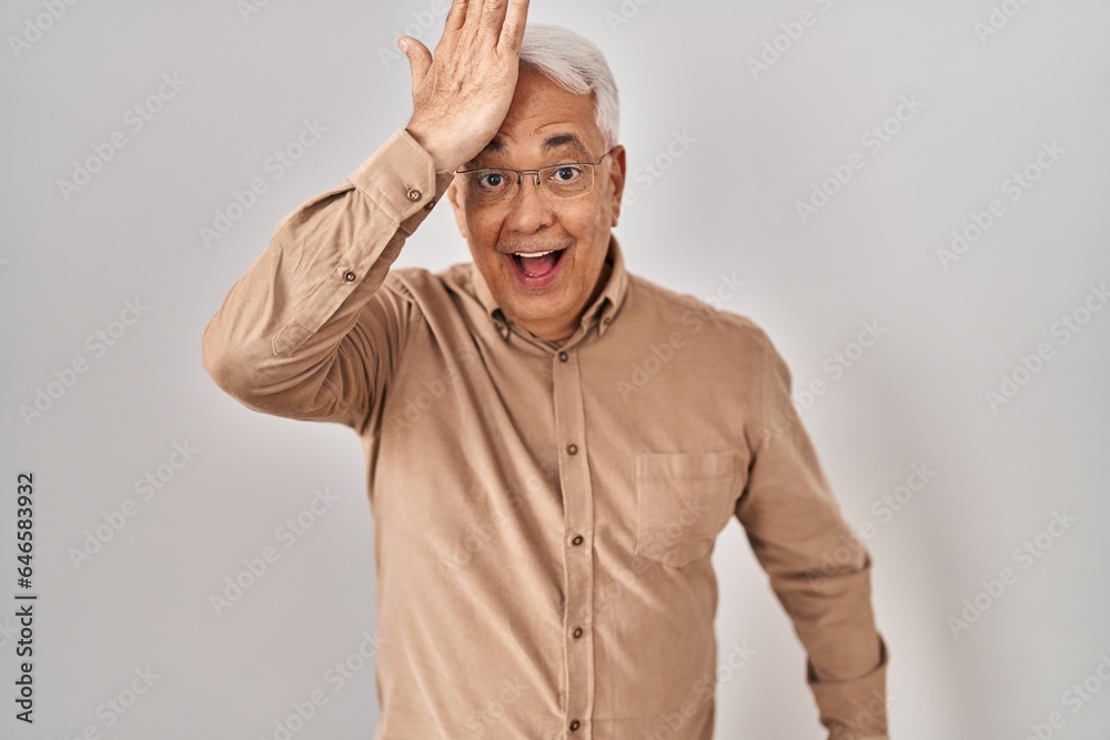 Hispanic senior man wearing glasses surprised with hand on head for mistake, remember error. forgot, bad memory concept. Hispanic senior man wearing glasses surprised with hand on head for mistake, remember error. forgot, bad memory concept.
