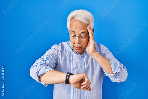 Hispanic senior man wearing glasses looking at the watch time worried, afraid of getting late