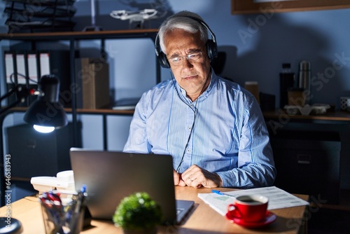 Hispanic senior man wearing call center agent headset at night depressed and worry for distress, crying angry and afraid. sad expression.
