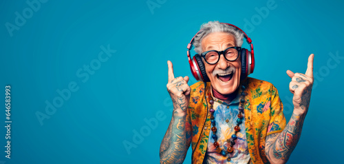 A happy hippie and cool grandfather, original style and tattoos, wearing headphones enjoying music, pointing his fingers up. Active and fun lifestyle concept for seniors: Sunset of life in colors photo