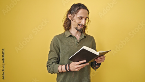 Young hispanic man reading book smiling over isolated yellow background