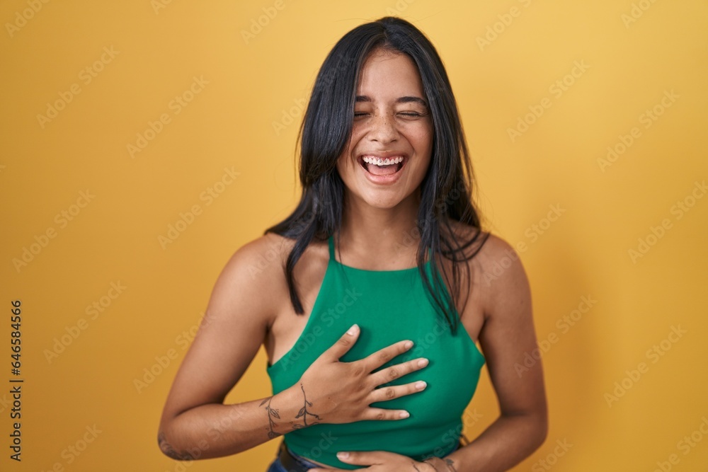 Obraz premium Brunette woman standing over yellow background smiling and laughing hard out loud because funny crazy joke with hands on body.