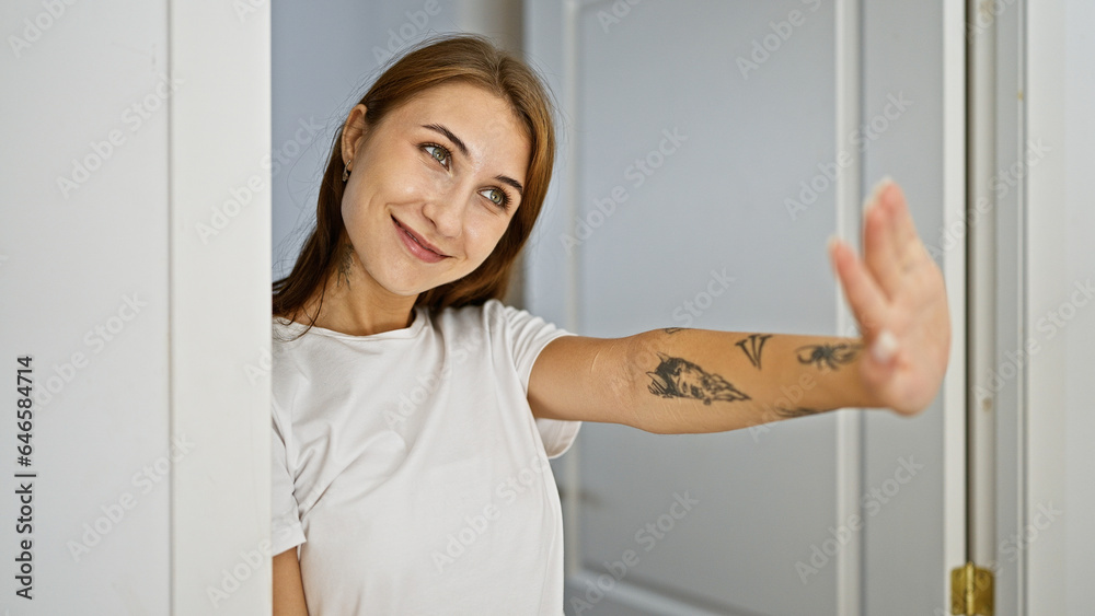 Young woman leaning on door saying hello with hand smiling at home Young woman leaning on door saying hello with hand smiling at home
