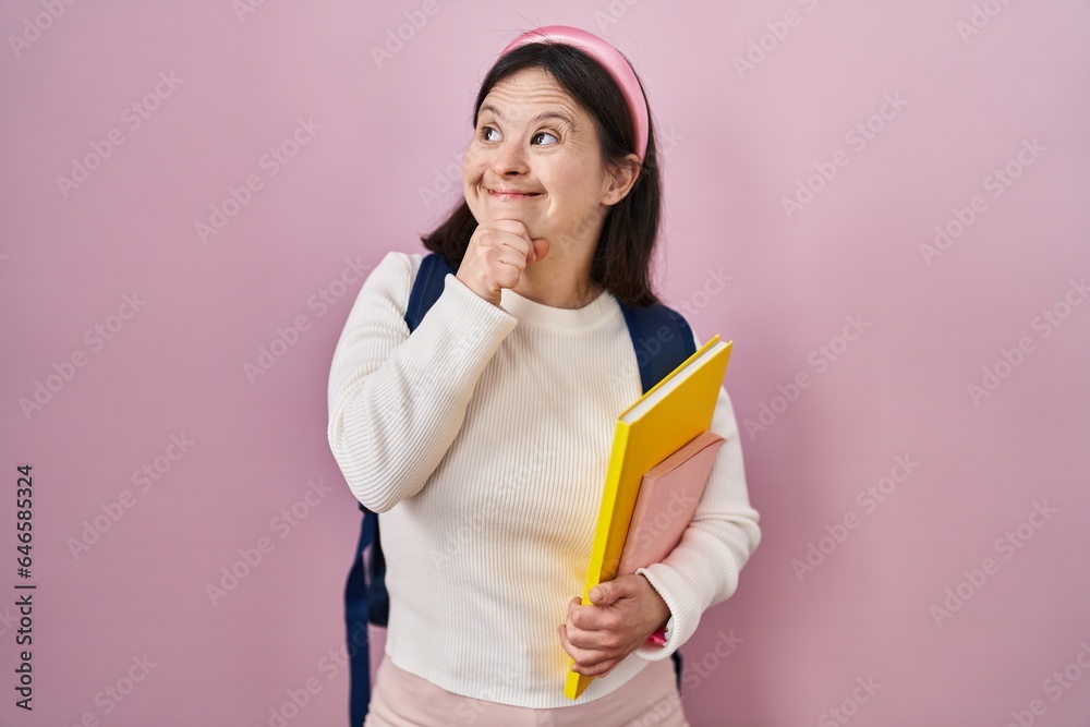 Woman with down syndrome wearing student backpack and holding books thinking worried about a question, concerned and nervous with hand on chin Woman with down syndrome wearing student backpack and holding books thinking worried about a question, concerned and nervous with hand on chin