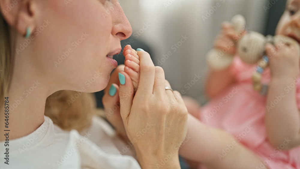 Mother and daughter sitting on sofa playing together kissing feet at home Mother and daughter sitting on sofa playing together kissing feet at home