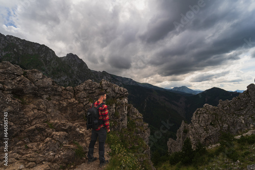 A man in a shirt with a briefcase behind his back is hiking in the Tatra mountains on a summer evening, the sky with thick clouds.