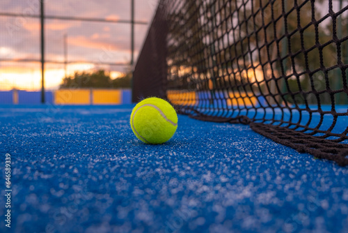 paddle tennis ball near the net on a blue paddle tennis court at sundown, racket sports concept © Vic