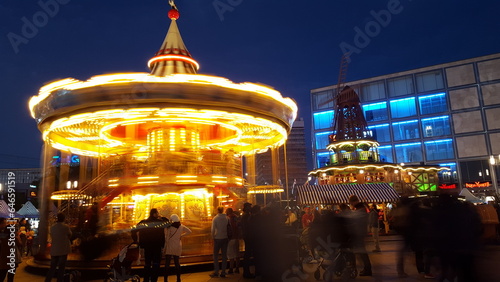 A vibrant carousel illuminates the night sky, its colorful lights reflecting off the excited faces of the people gathered around it..