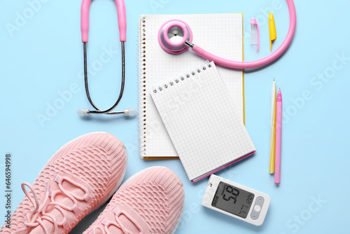 Blank notebooks with glucometer, sneakers and stethoscope on blue background. Diabetes concept