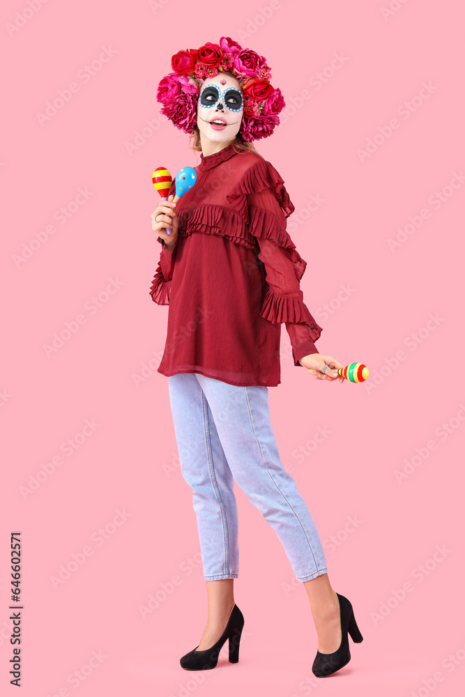 Young woman with painted skull and maracas on pink background. Mexico's Day of the Dead (El Dia de Muertos) celebration Young woman with painted skull and maracas on pink background. Mexico's Day of the Dead (El Dia de Muertos) celebration