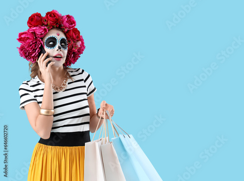 Young woman with shopping bags talking by mobile phone on blue background. Mexico's Day of the Dead (El Dia de Muertos) celebration