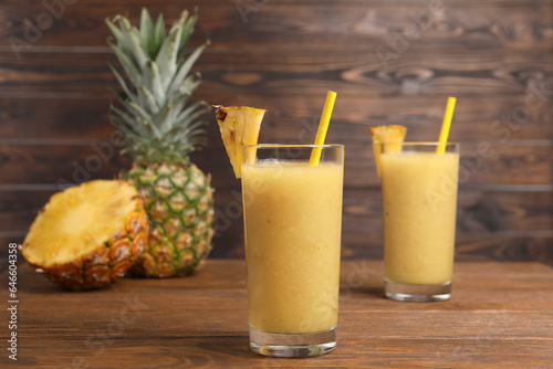 Tasty pineapple smoothie, whole and cut fruit on wooden table