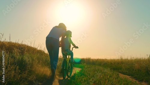 Child dream of riding bike. Mother teaches her child to keep balance while sitting on bicycle. Mom teaches her child, little daughter to ride bike, sunset. Family life, mom, baby, parental support.