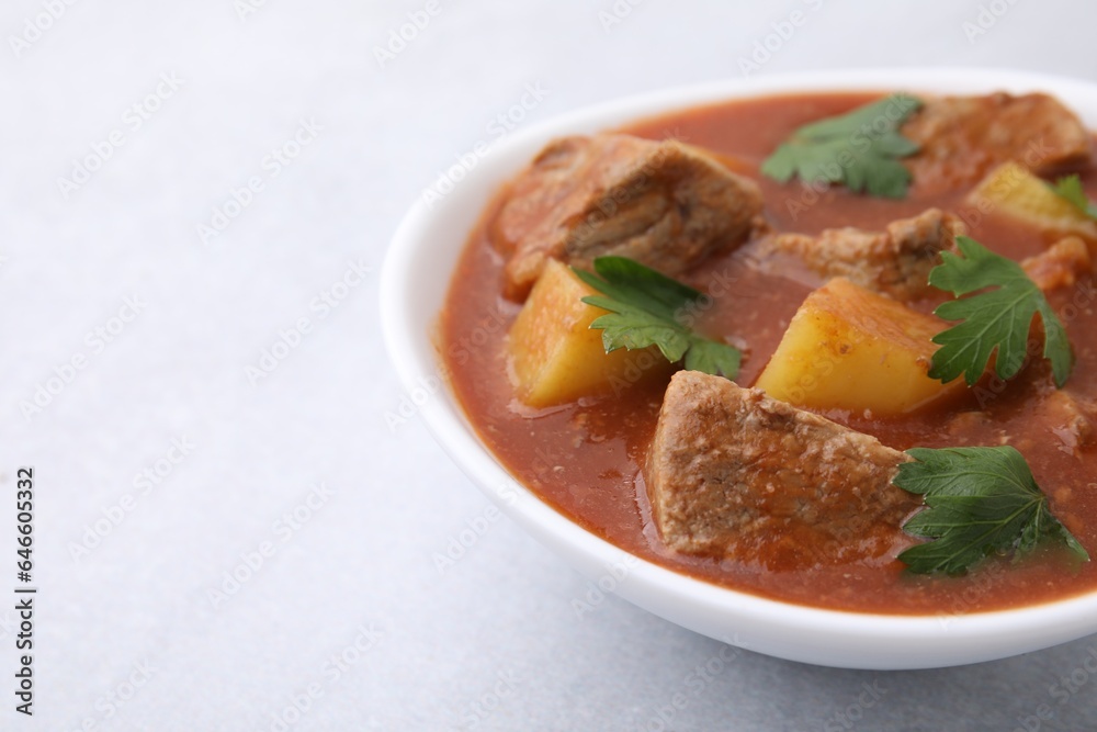 Delicious goulash in bowl on light grey table, closeup. Space for text Delicious goulash in bowl on light grey table, closeup. Space for text