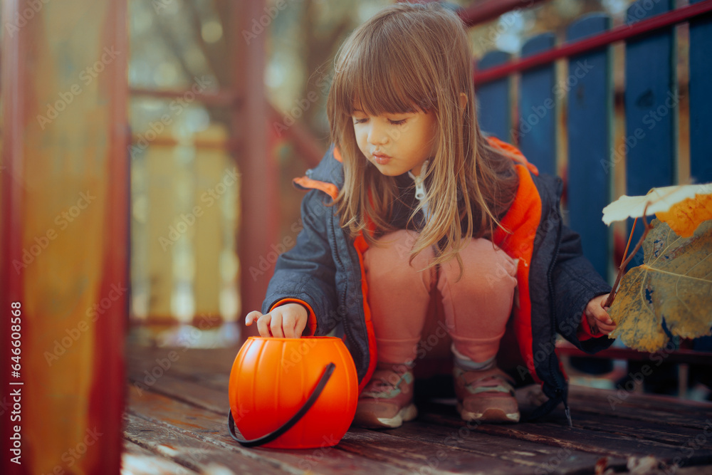 Fototapeta premium Little Girl with Halloween Candy Bucket Playing with a Cat. Child having fun outdoors with his pet going trick or treat 
