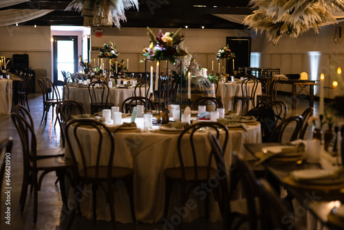 Wedding reception table with farmhouse elements and black vases with flowers and lit candles and place settings