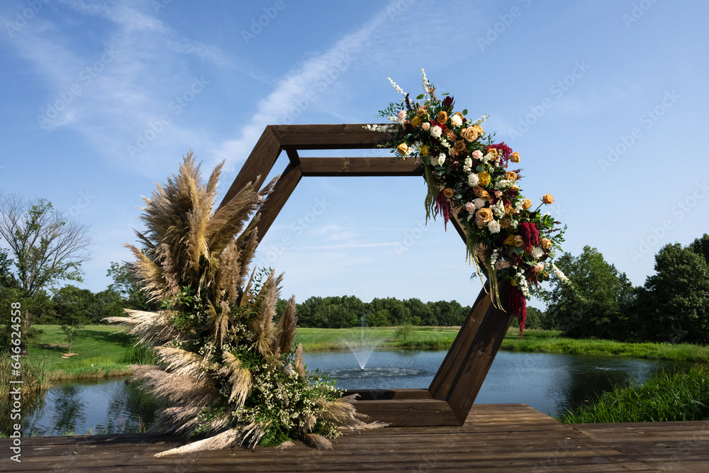 Fototapeta premium wedding arch with pampas and flowers adorning with a water founding in background