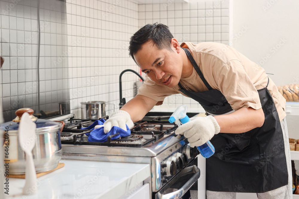 Man cleaning kitchen stove with detergent spray bottle and cloth