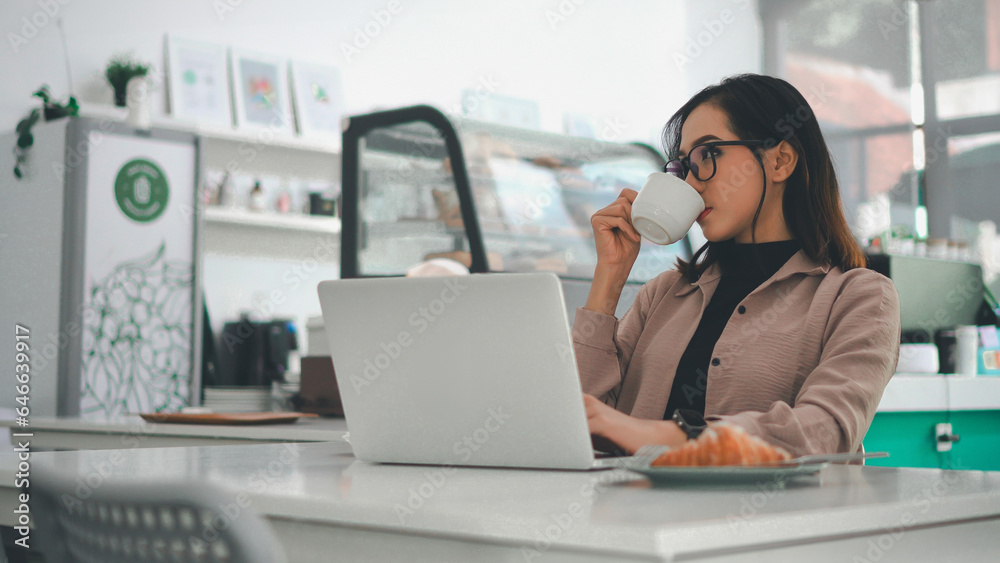 Asian business woman working on a laptop while enjoying a cup of coffee in a cafe
Asian business woman working on a laptop while enjoying a cup of coffee in a cafe
