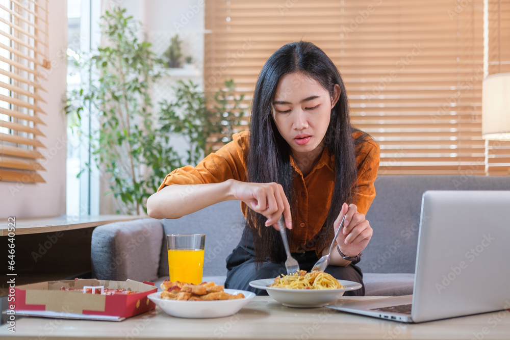 Cheerful young woman sitting on sofa and eating tasty spaghetti. Domestic life and food concept..