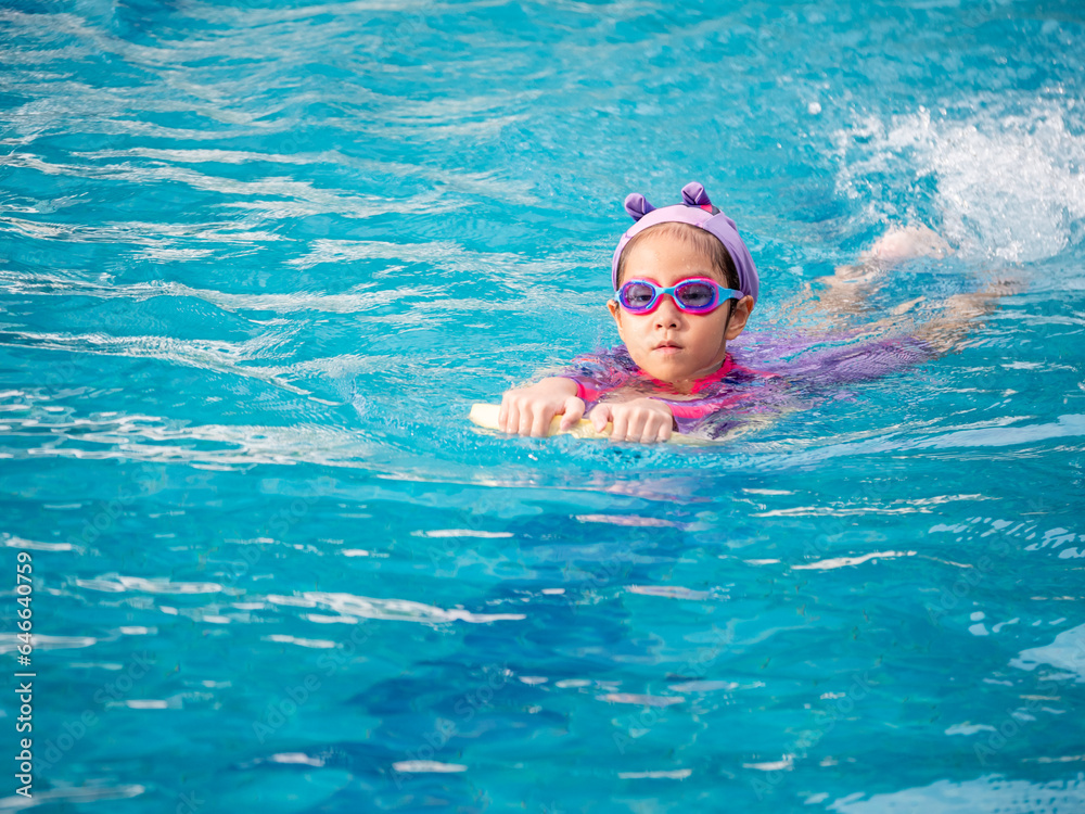 Asian child or kid girl wearing swimming suit to learning on swimming pool , learn and training swim on kick board