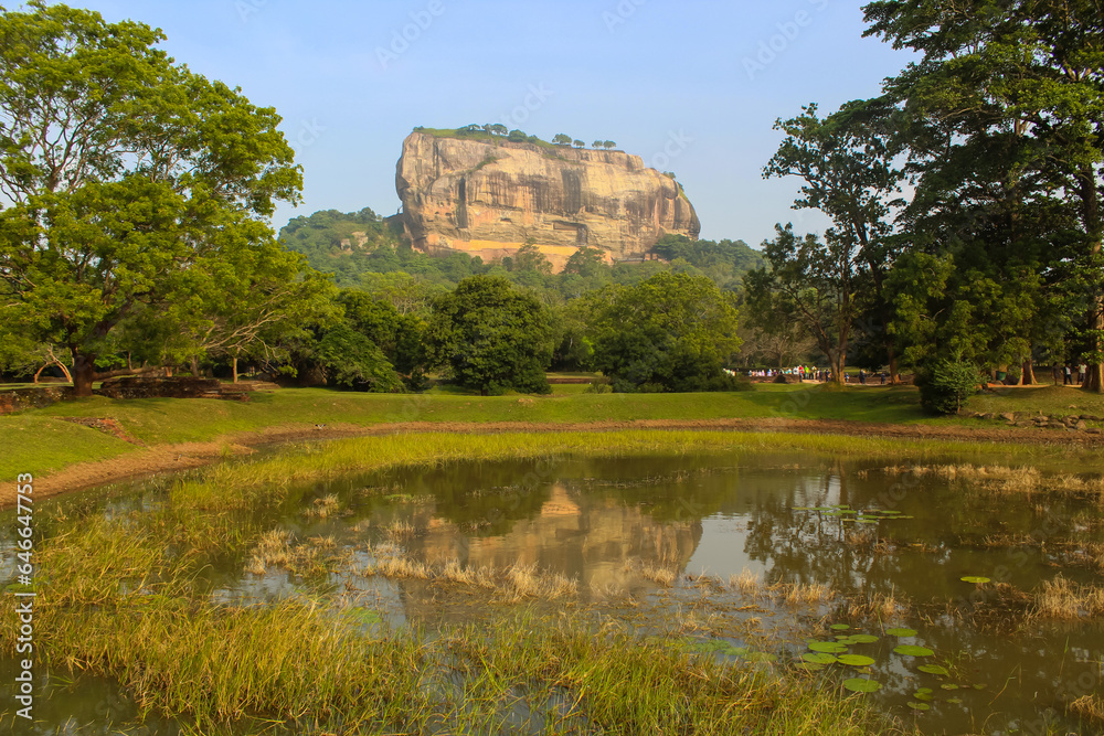 Sigiriya Lion Rock fortress behind the trees with the pond on the foreground