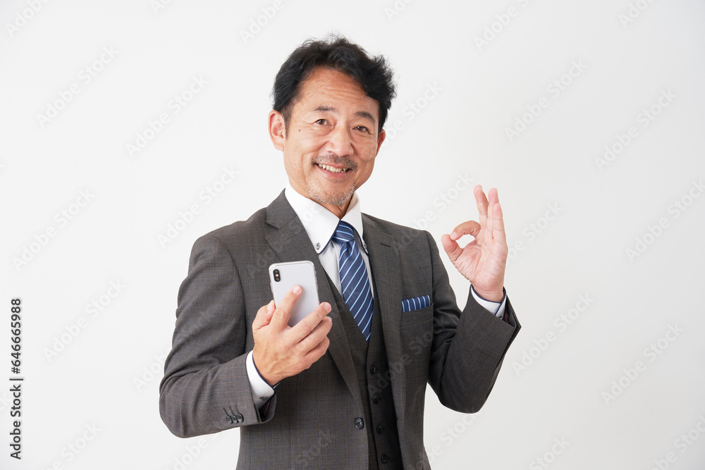 スマホを持ってOKポーズをする中年のビジネスマン 白背景 スマホを持ってOKポーズをする中年のビジネスマン 白背景