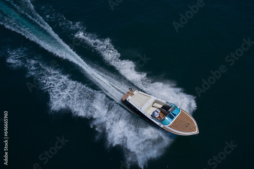 Luxury wooden big speedboat fast moving on dark water top view. Boat movement on the water. Motor boat in motion. Expensive wooden big boat with people moving on the water aerial view. © Berg