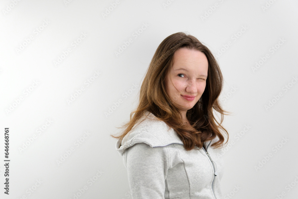 young teenage girl turns to camera smiles and blinks first with right and then with left eye light smile playfulness joke good mood. in studio hair developing chic hairstyle well-groomed beauty young teenage girl turns to camera smiles and blinks first with right and then with left eye light smile playfulness joke good mood. in studio hair developing chic hairstyle well-groomed beauty