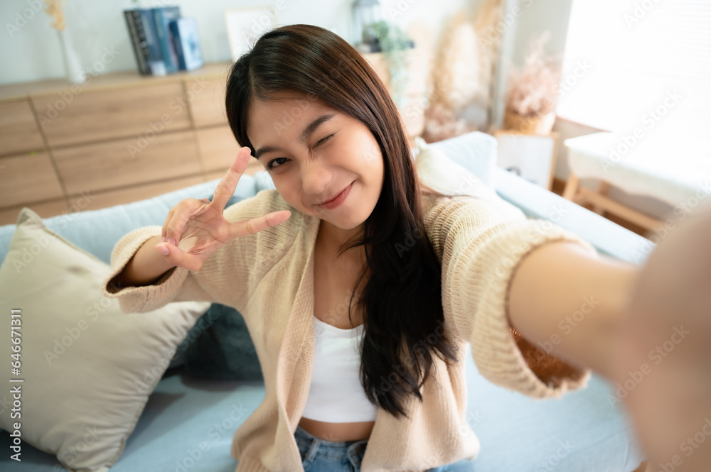 Pretty young asian female with big smile sitting at living room. She having fun taking light cheerful selfie on blurred background Pretty young asian female with big smile sitting at living room. She having fun taking light cheerful selfie on blurred background
