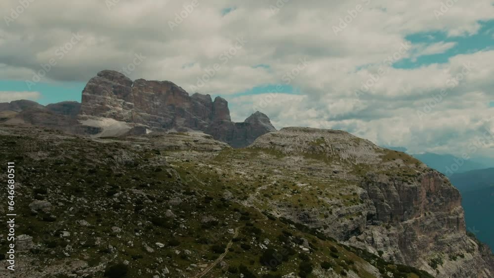 Drone shot with tall steep rocky mountains and partly clouded sky in the background, cinematic color grade Drone shot with tall steep rocky mountains and partly clouded sky in the background, cinematic color grade