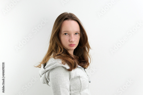 a very strict displeased look of a teenage girl turned her head into the frame looked sternly beautiful hairstyle gray hooded sweatshirt. on a white background © Oleksandra