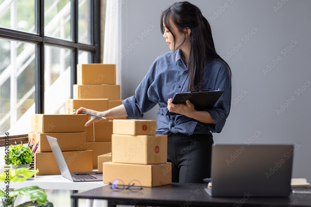Young Asian woman SME small business owner online shopping at home. taking note of orders from customers with laptop and phone. SME entrepreneur or freelance life style concept.