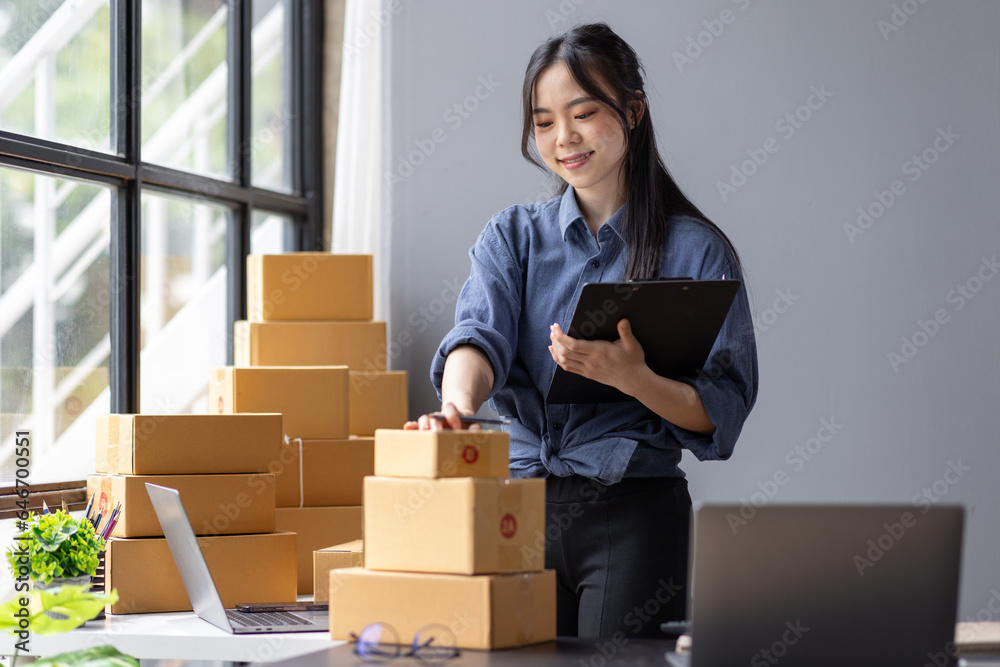 Young Asian woman SME small business owner online shopping at home. taking note of orders from customers with laptop and phone. SME entrepreneur or freelance life style concept. Young Asian woman SME small business owner online shopping at home. taking note of orders from customers with laptop and phone. SME entrepreneur or freelance life style concept.