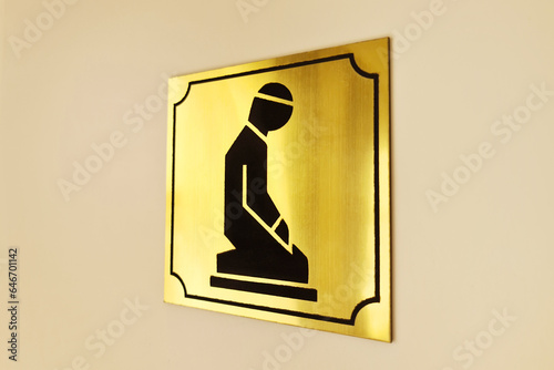 A plate with a drawing of a praying person on the door of a prayer room for representatives of the Islamic religion.